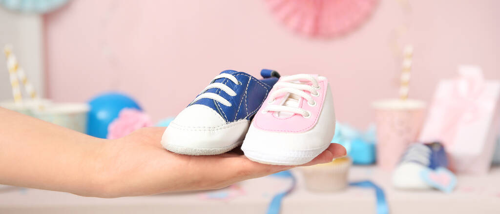 A woman holding baby shoes in blue and pink at a gender reveal party